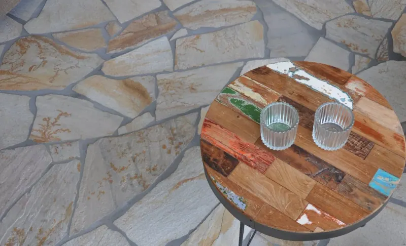 Vista cercana de un piso irregular gris claro y dorado junto a una mesa redonda de madera con dos vasos