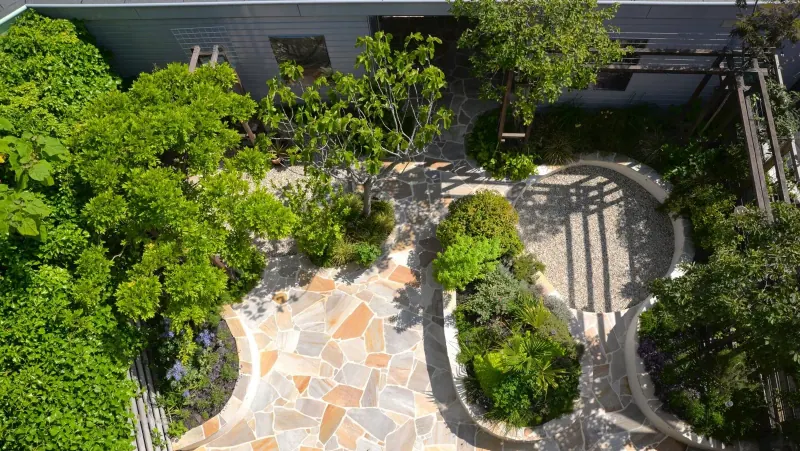 Vista superior de un jardín con senderos de piedra irregular y un espacio circular de gravilla