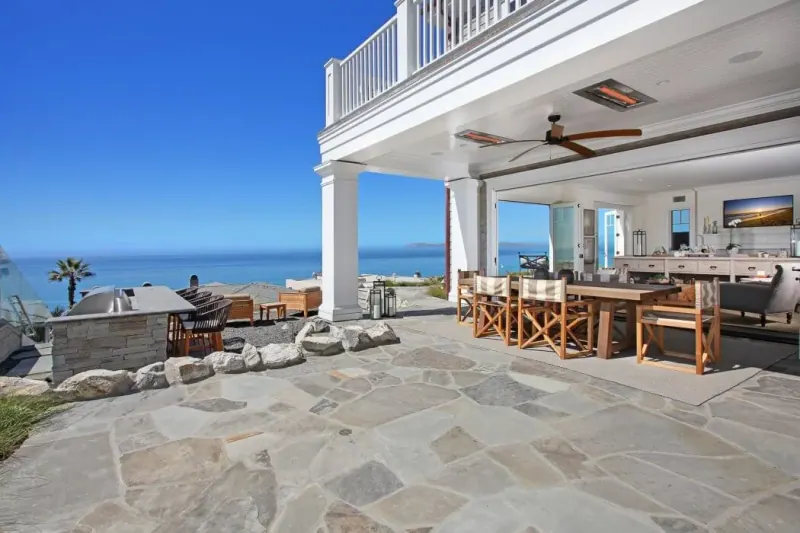 Terraza frente al mar con piso de piedra irregular gris y comedor junto a una casa blanca