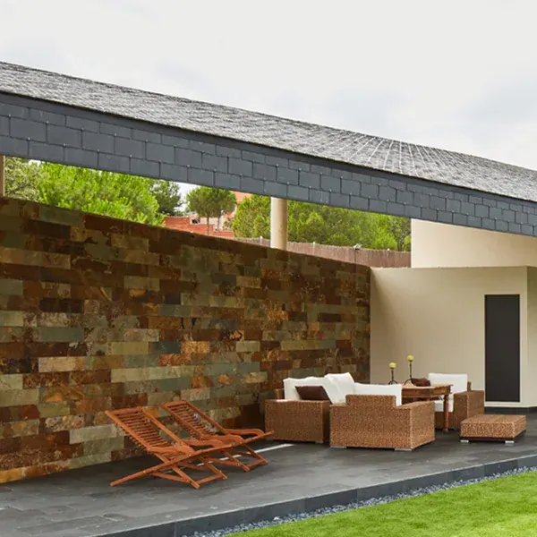 Terraza cubierta con muro de piezas horizontales multicolores y muebles de fibras