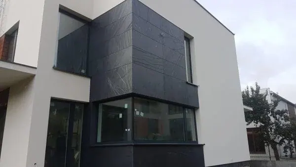 Volumen de una fachada contemporánea con placas oscuras de pizarra y ventanas en esquina