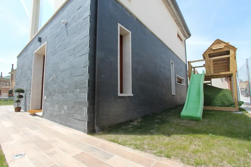 Fachada de una vivienda revestida con piezas rectangulares de pizarra gris junto a un jardín