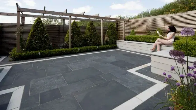 Patio con piso de pizarra gris, franjas claras, pérgola y jardineras