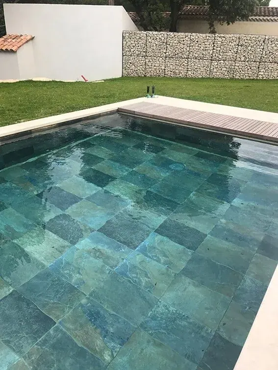 Referencia de piscina revestida con piezas de pizarra de distintos tonos bajo el agua